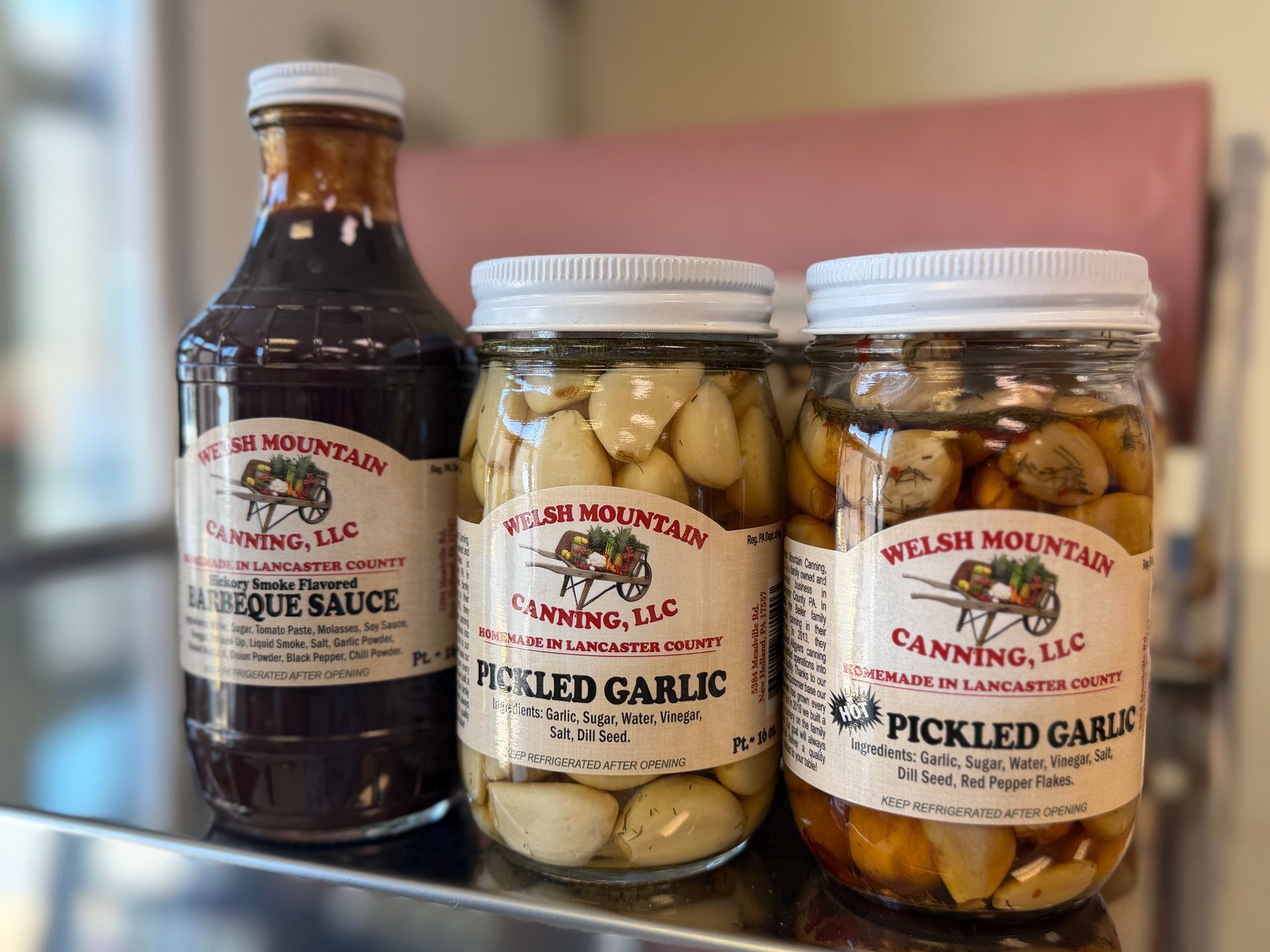 Three food jars on a counter: liquor sauce, pickled garlic, and pickled jalapeños with white lids
