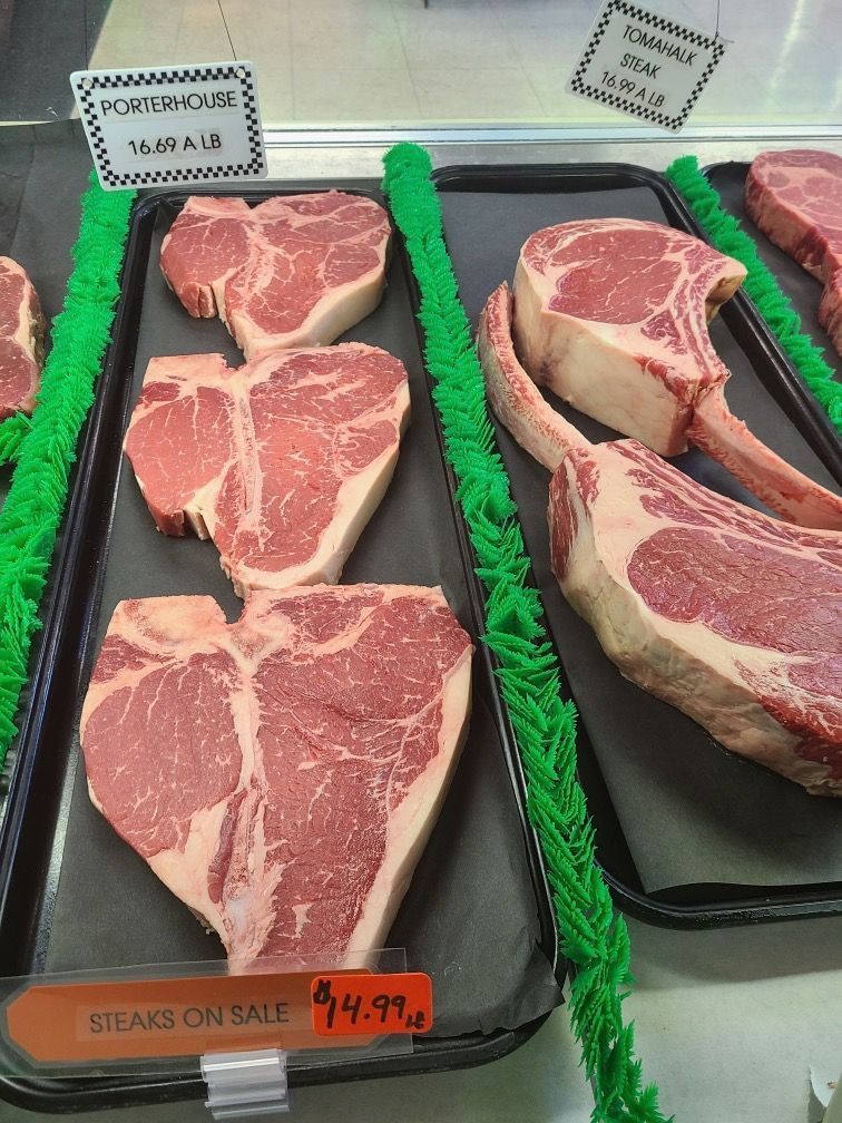 Display case with raw steaks on trays, labeled with prices and green garnish borders.