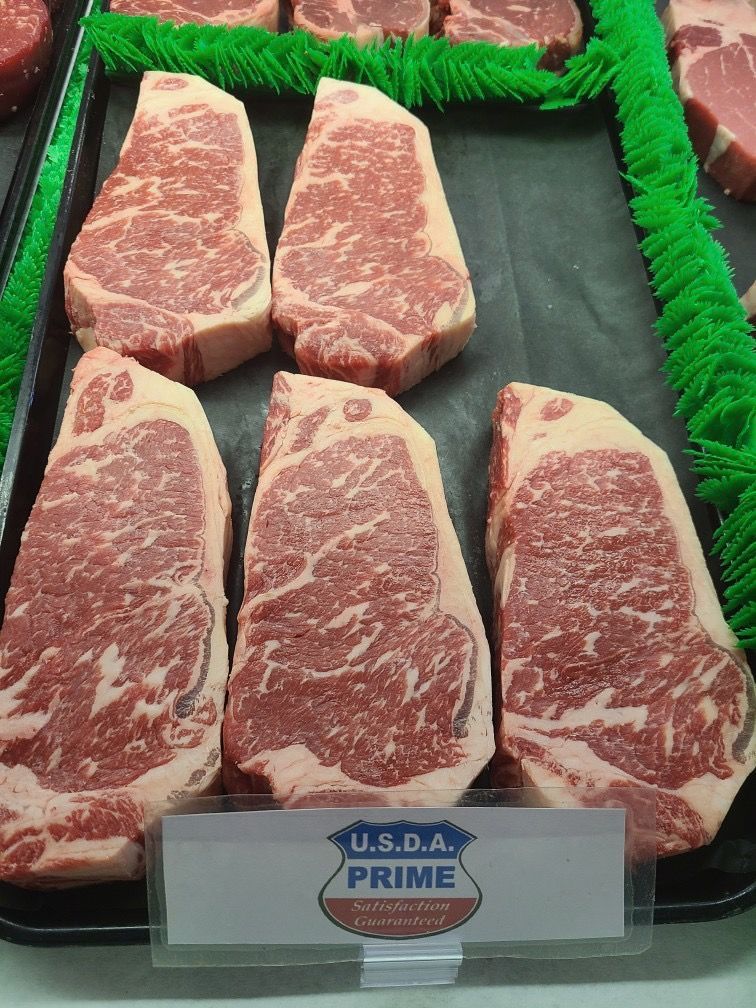 Five USDA Prime marbled beef steaks displayed in a meat case with green trim