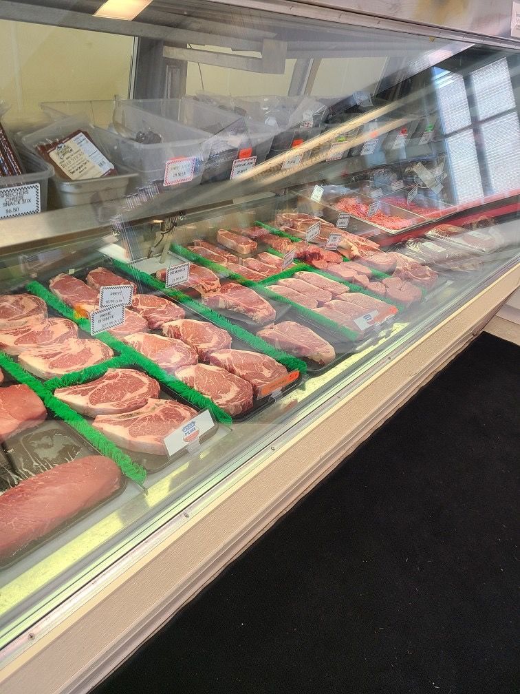 Butcher case with trays of raw meat wrapped in clear plastic and labeled in a grocery store display.