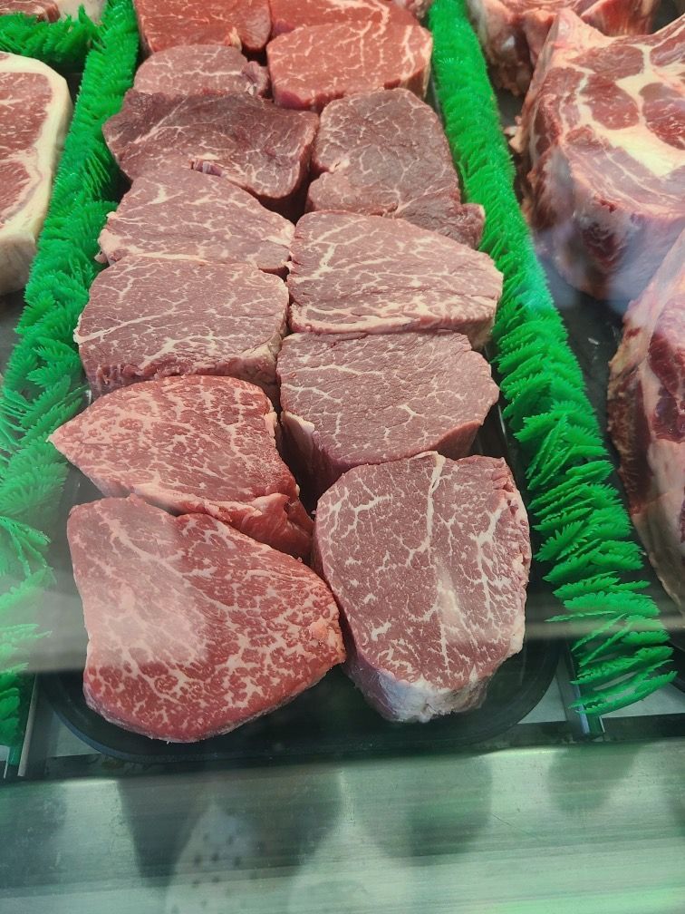 Raw beef steaks arranged in a tray with green garnish, displayed in a deli case