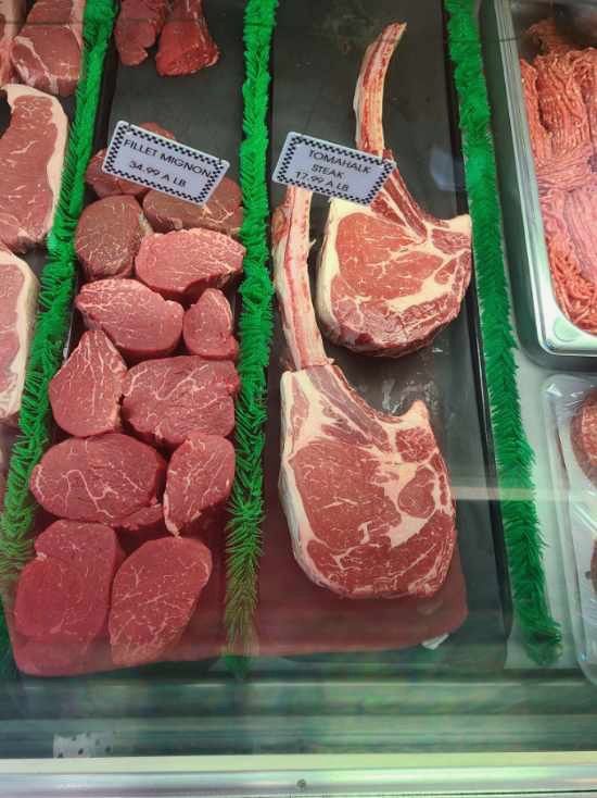 Butcher display case with assorted raw steaks and sliced meats on green grass-like lining