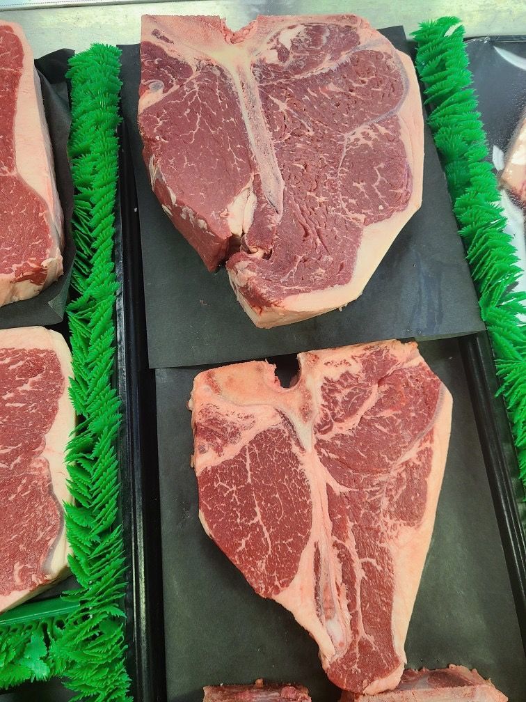 Raw ribeye steaks displayed on black trays with green garnish in a butcher case