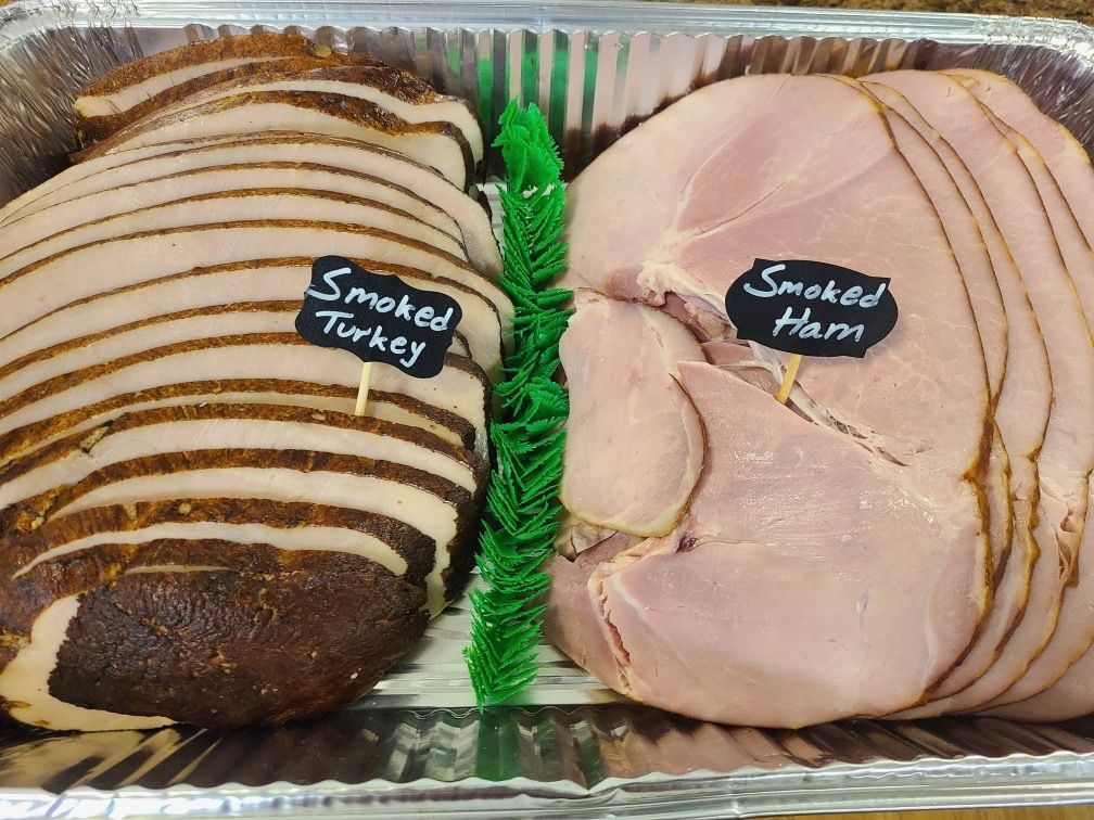 Sliced smoked turkey and smoked ham displayed side by side in a tray with labels