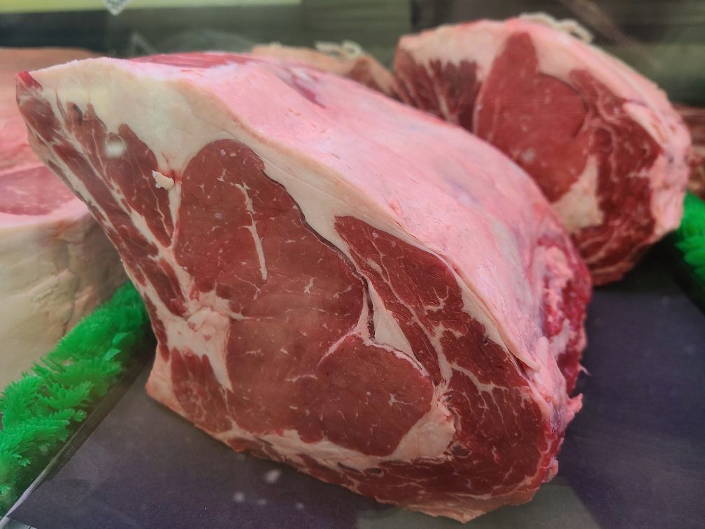 Raw marbled meat cuts on a butcher’s counter, with a large red and white roast in the foreground