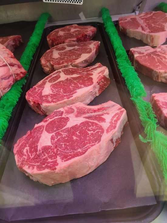 Raw marbled steaks displayed in a butcher case on green dividers