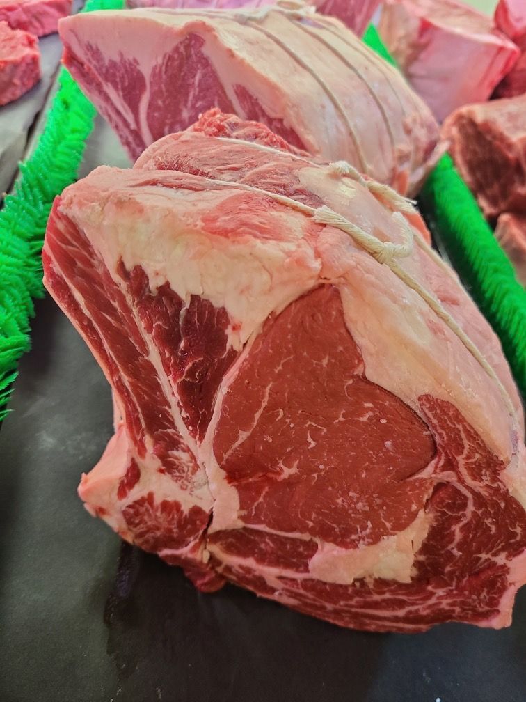 Raw ribeye steaks displayed on a black tray with green garnish