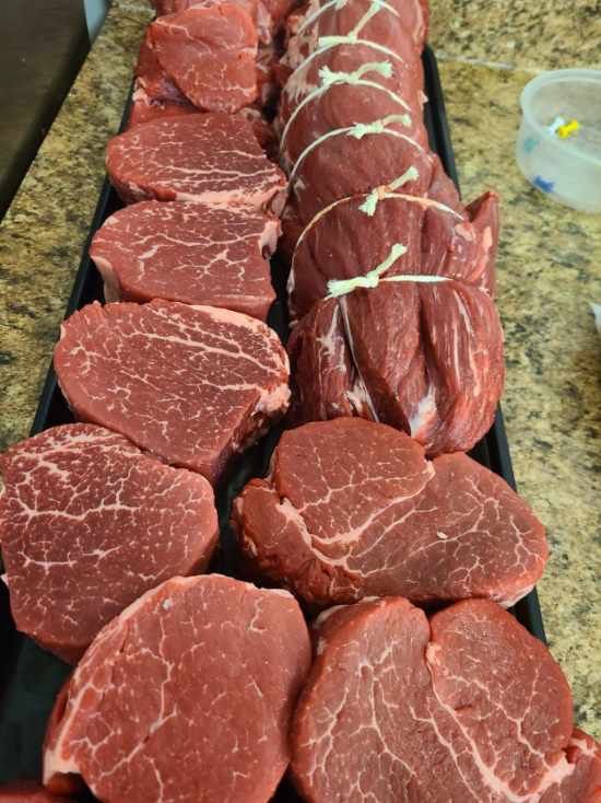 Tray of raw beef cuts and tied roasts on a kitchen counter