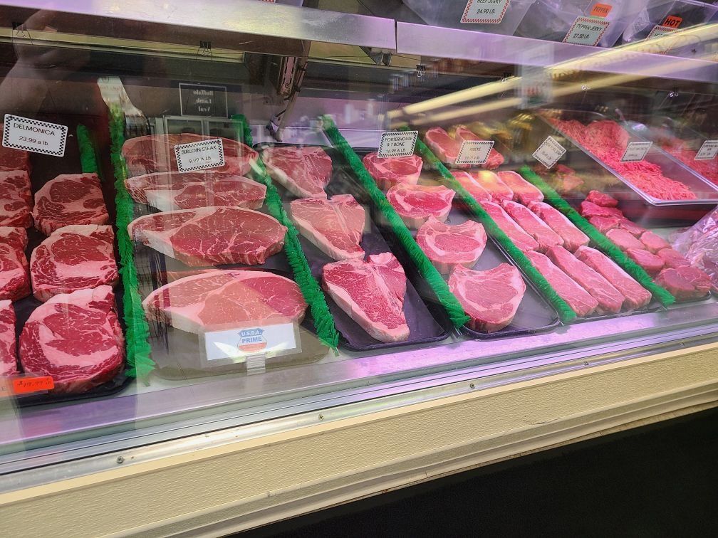 Meat display case with assorted raw steaks and cuts arranged in rows under bright store lighting