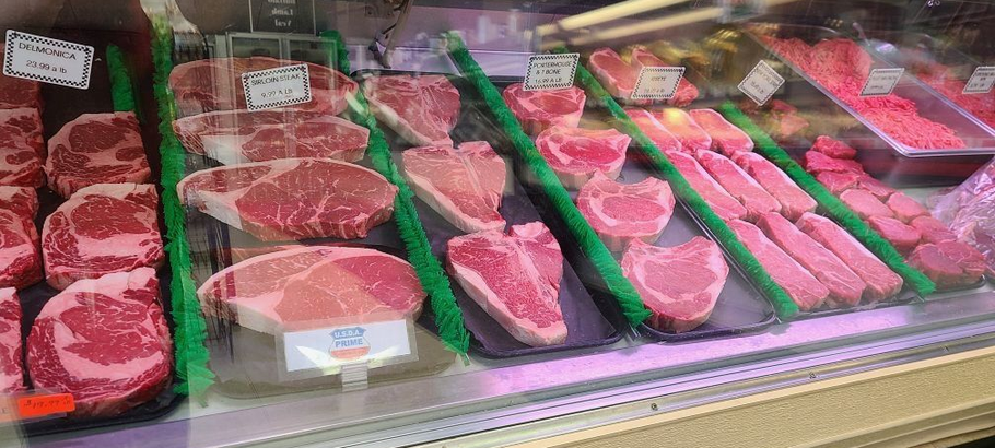 Butcher counter with various raw steaks and cuts of meat displayed in trays under glass