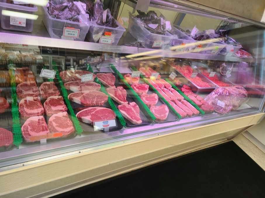 Butcher display case with assorted raw steaks and cuts of meat in plastic trays under glass.