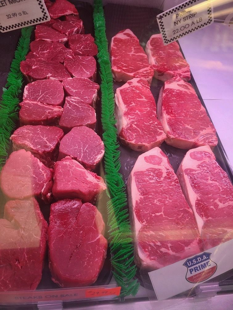 Display case of raw beef cuts arranged in trays, with bright red meat and marbling.