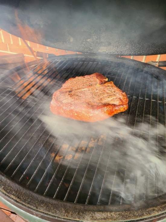 Steak sizzling on a grill with smoke and orange flames in the background