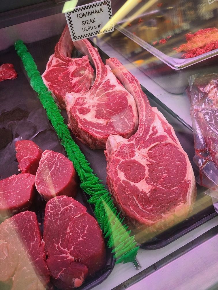 Display case with assorted raw beef steaks and roasts, including marbled ribeye cuts.
