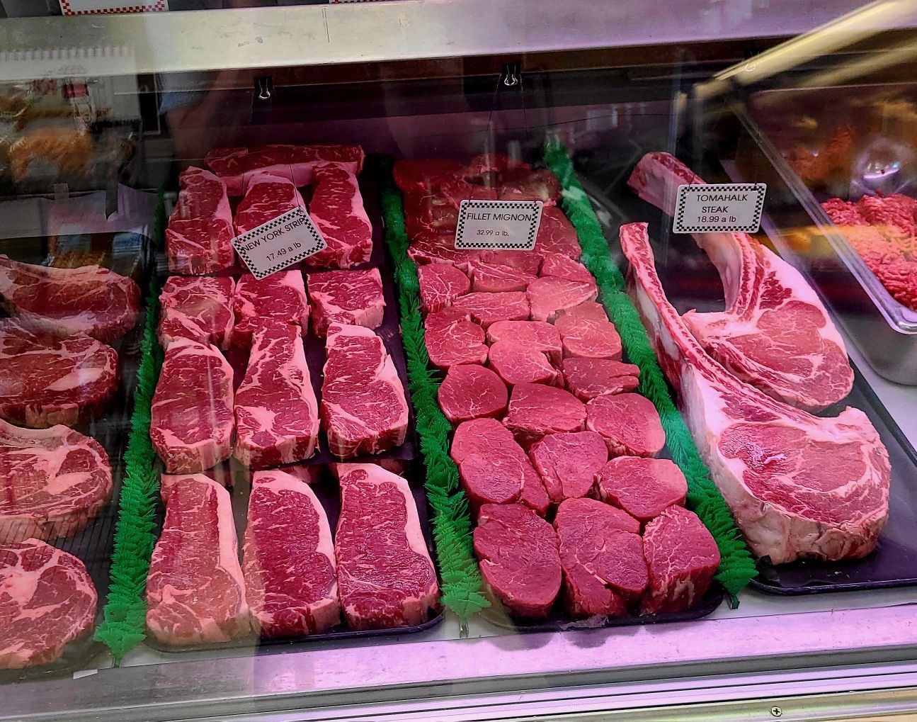 Butcher shop display of raw steaks and cuts of meat on trays behind glass, labeled with price signs