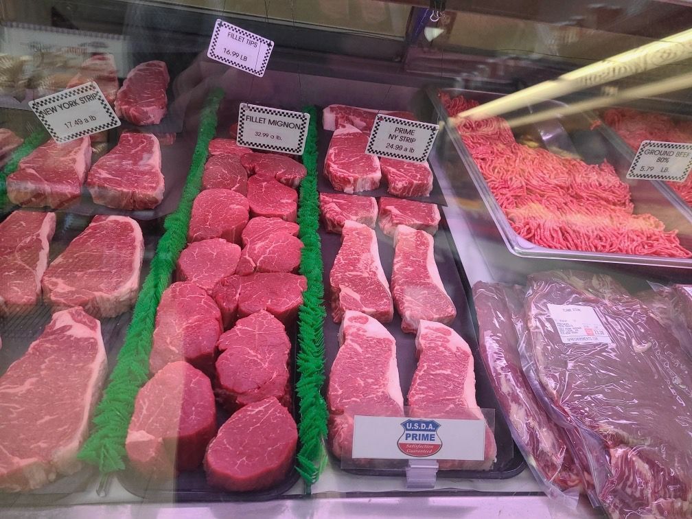Meat cuts displayed in a butcher case with labels and price tags.
