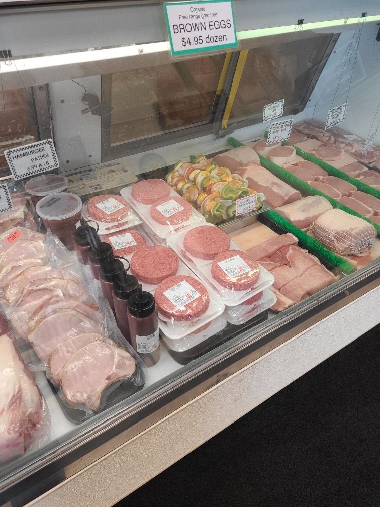 Butcher case with packaged raw meats, deli trays, and produce behind a glass display counter