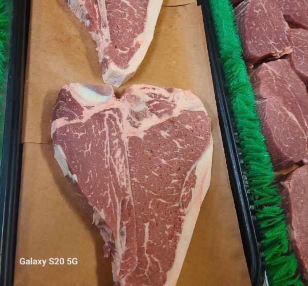 Heart-shaped raw steak in a butcher display case, with other meat cuts nearby.