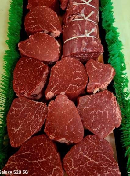Raw beef steaks arranged in a tray, with green garnish around the edges