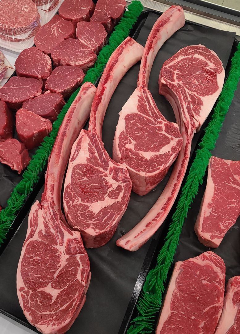 Assorted raw steaks displayed in a butcher case with green garnish divider strips