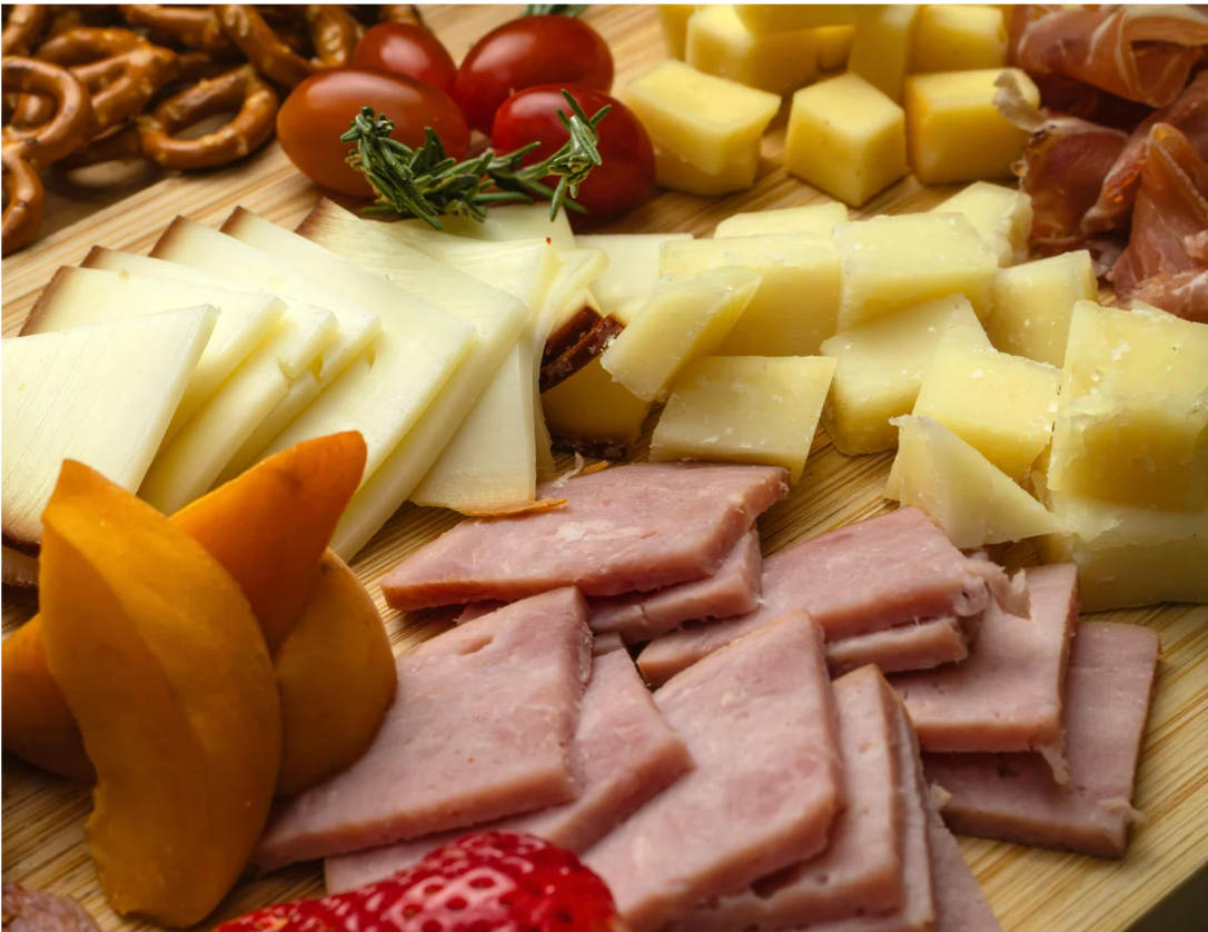 Cheese and cured meats arranged on a wooden board with grapes and tomatoes