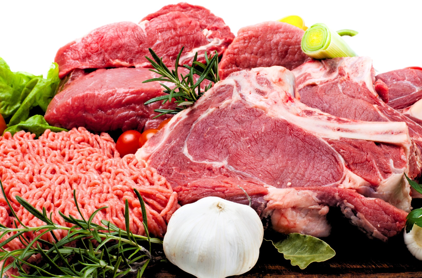 Assorted raw meats with herbs and garlic on a platter, including steaks, chops, and ground beef.