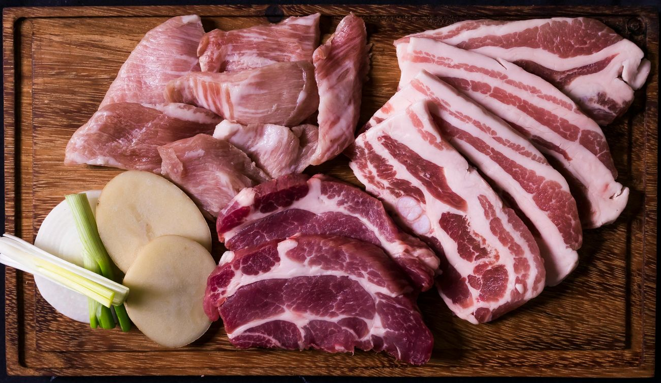Assorted raw pork cuts and green onions on a wooden cutting board