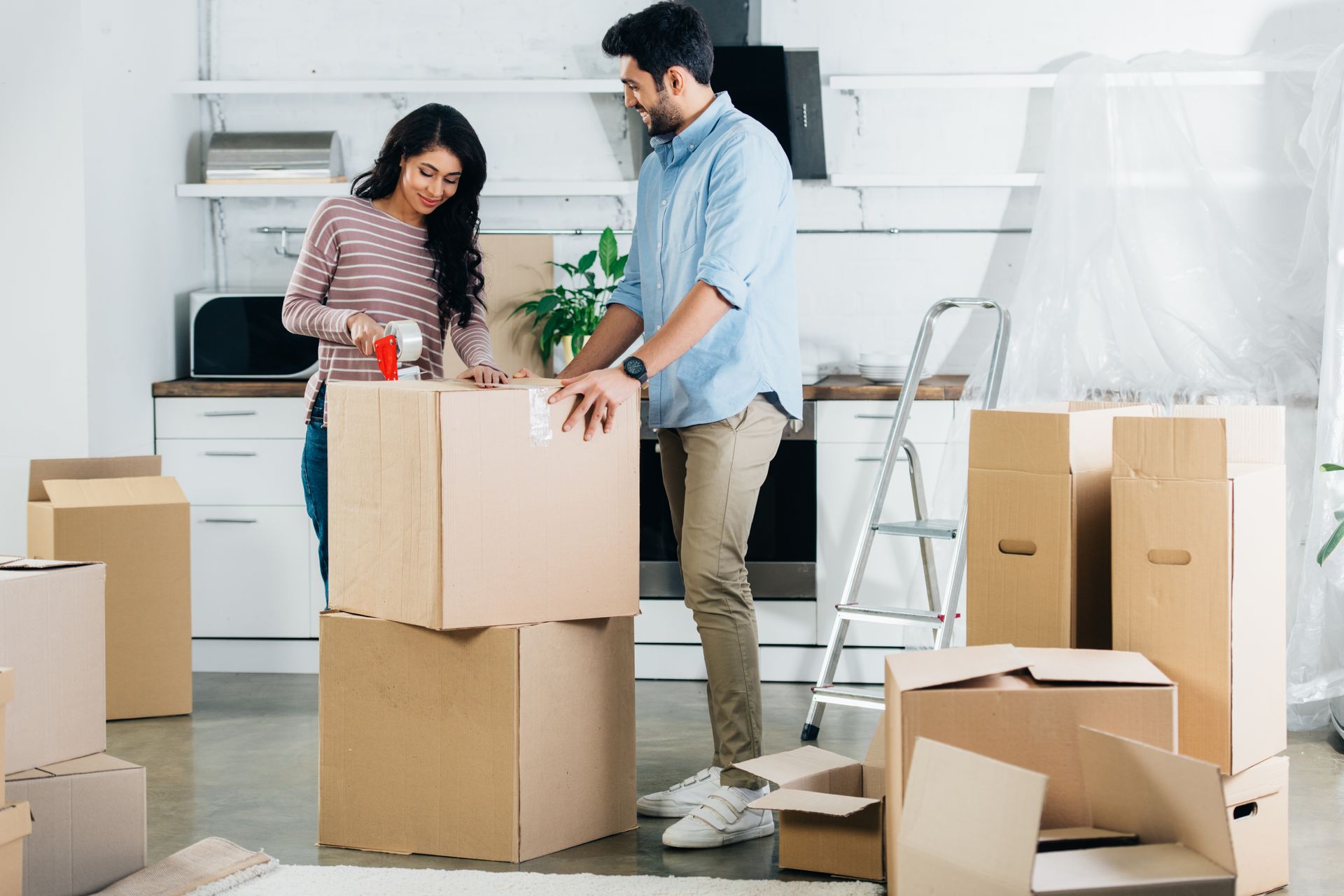 A couple taping shut a moving box after packing it up in their kitchen