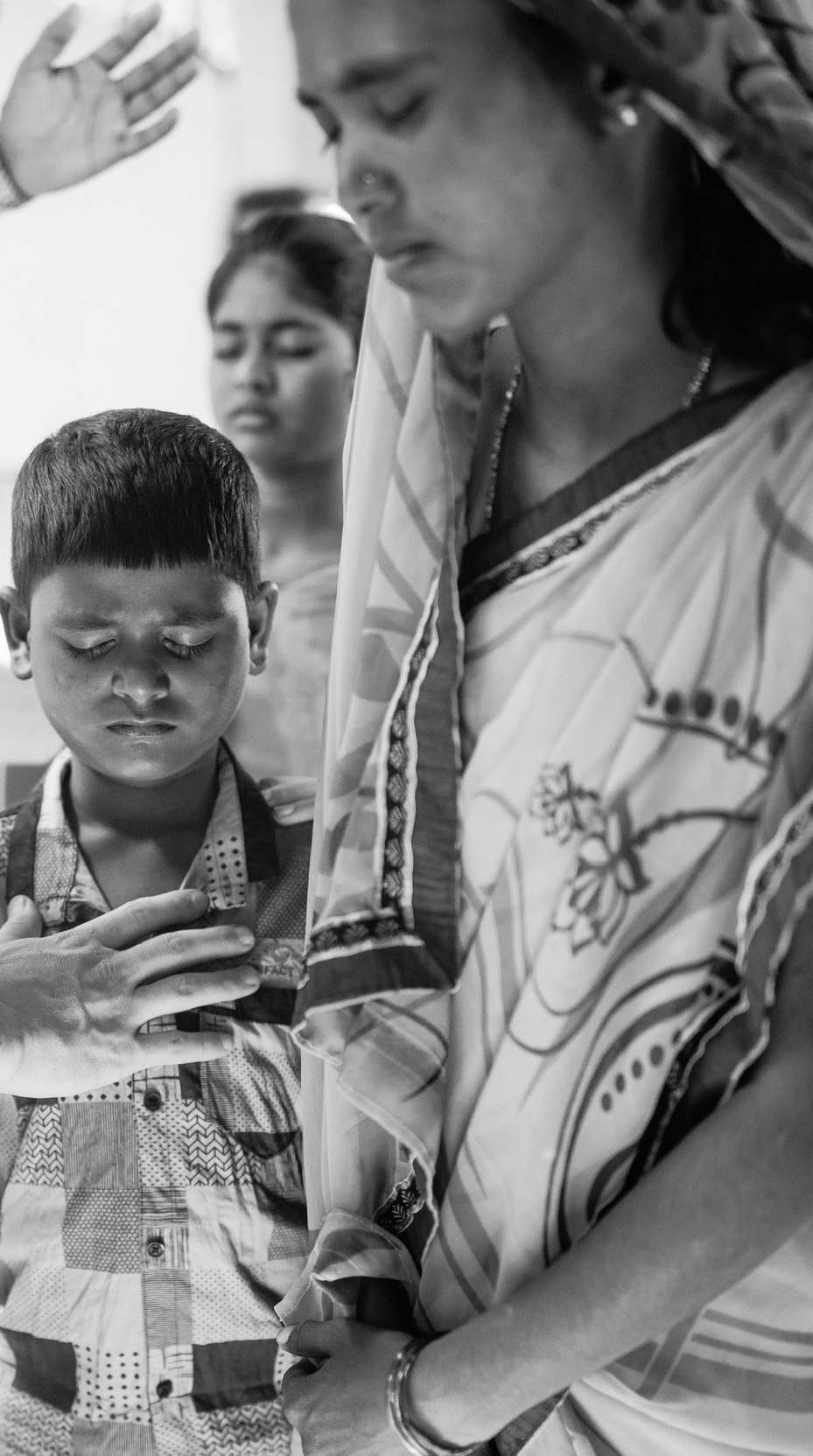 Woman in sari with boy and girl; woman has hands clasped, boy's head is bowed.