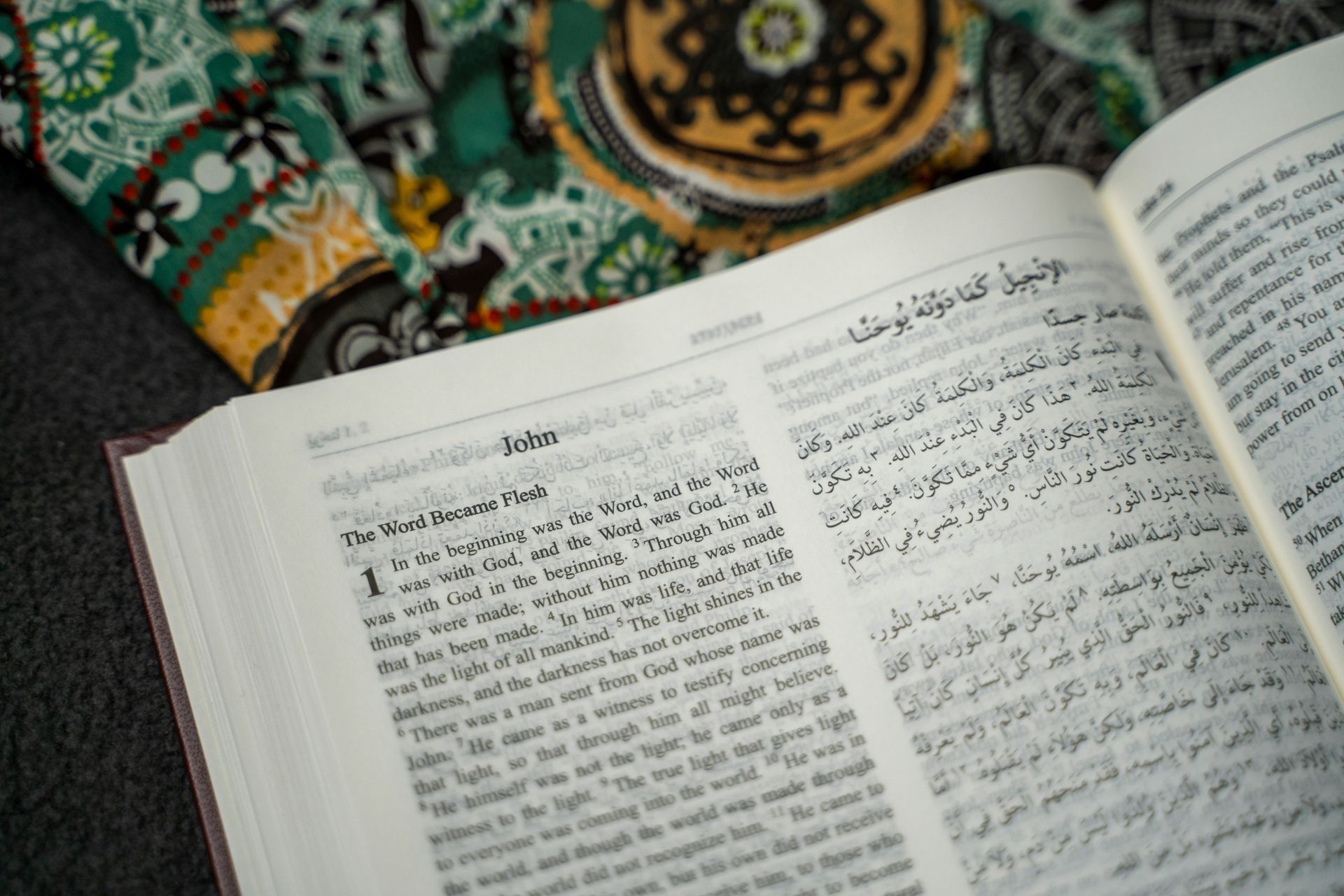 Open book with text in Arabic and English, resting on patterned fabric.