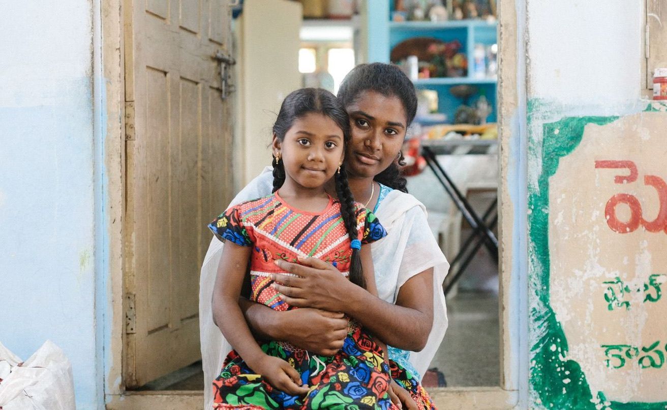 Woman and child embracing in doorway. Girl smiles; woman has arm around her.