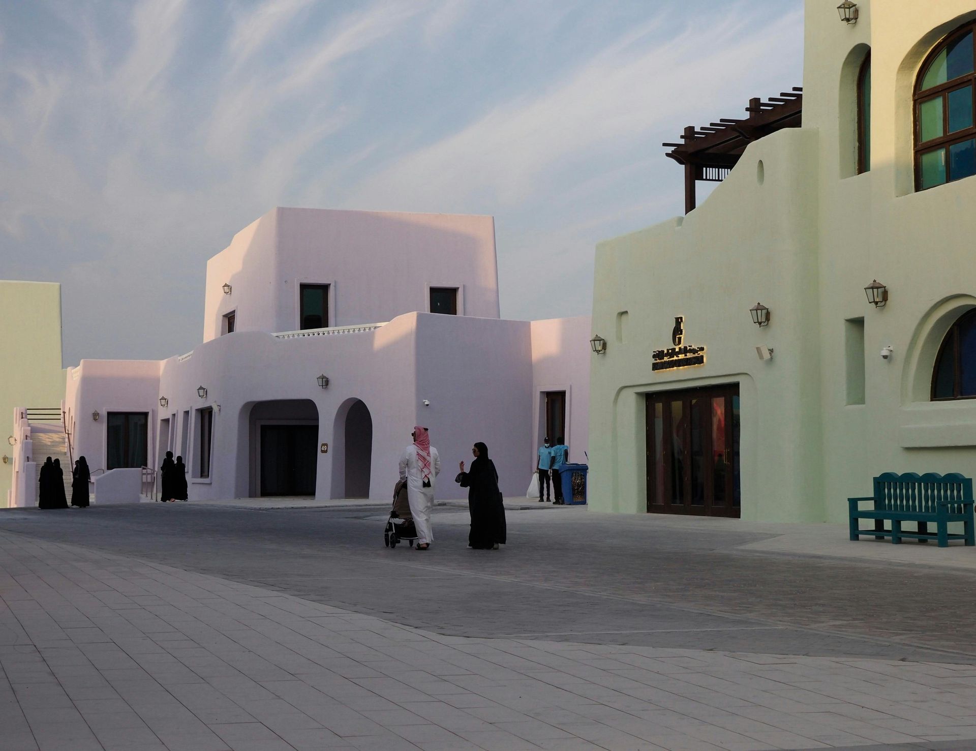 Buildings in Qatar, beige and pink, with people walking. Clear sky, outdoor setting.