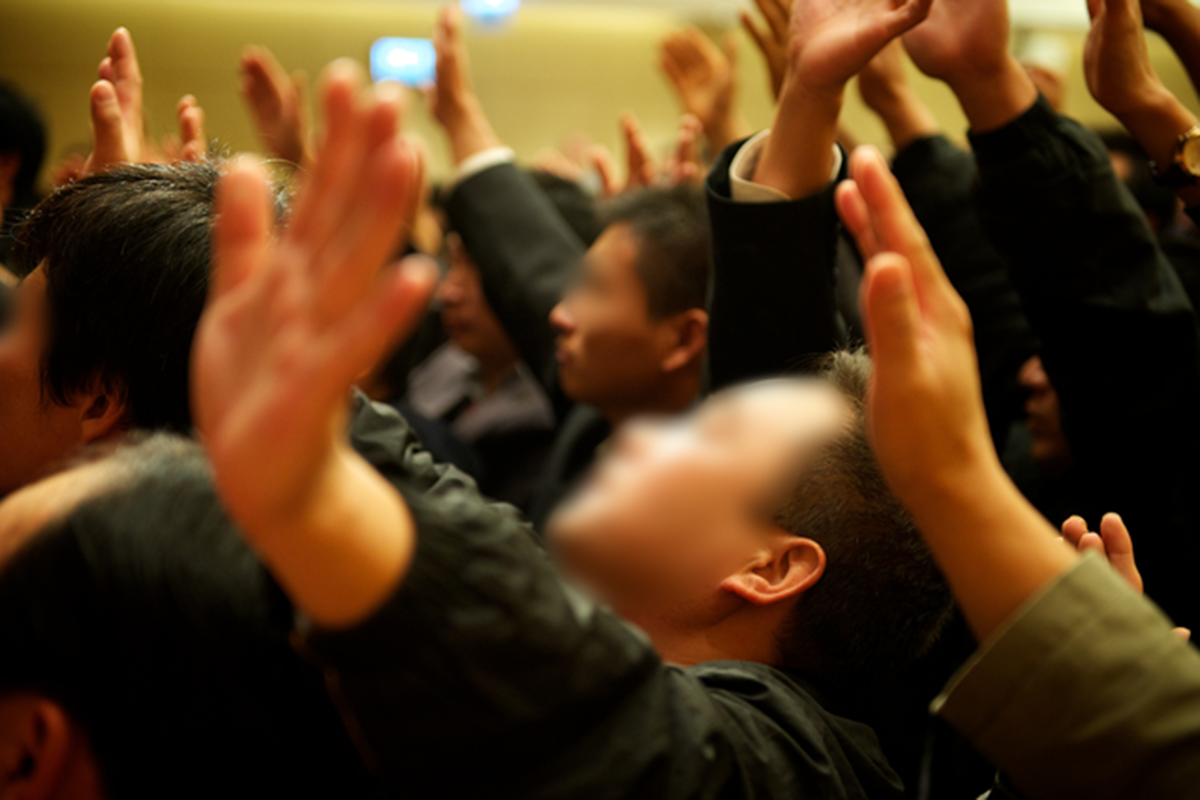 People with arms raised in a brightly lit room. Some faces are visible.