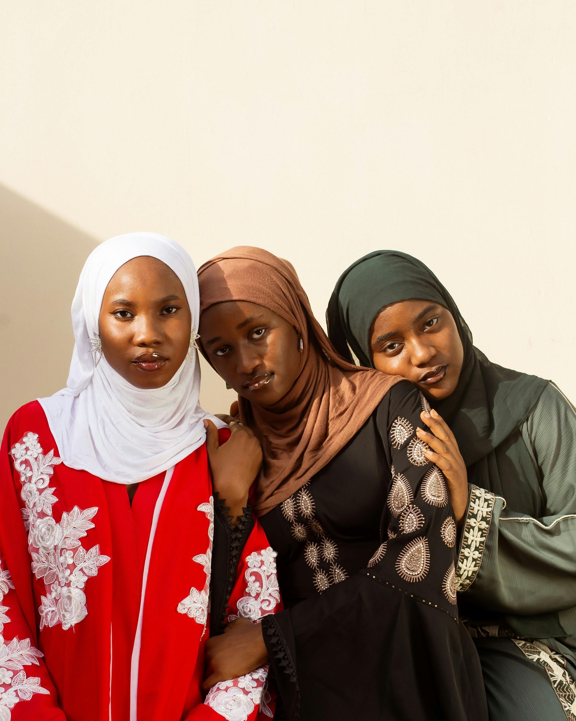 Three women in headscarves and dresses pose together against a neutral background.