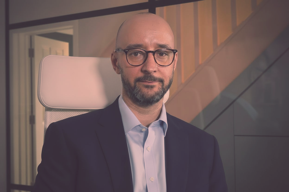 Justin Tate of The Exec Memo wearing glasses and suit, looking at the camera. He's in an office setting.