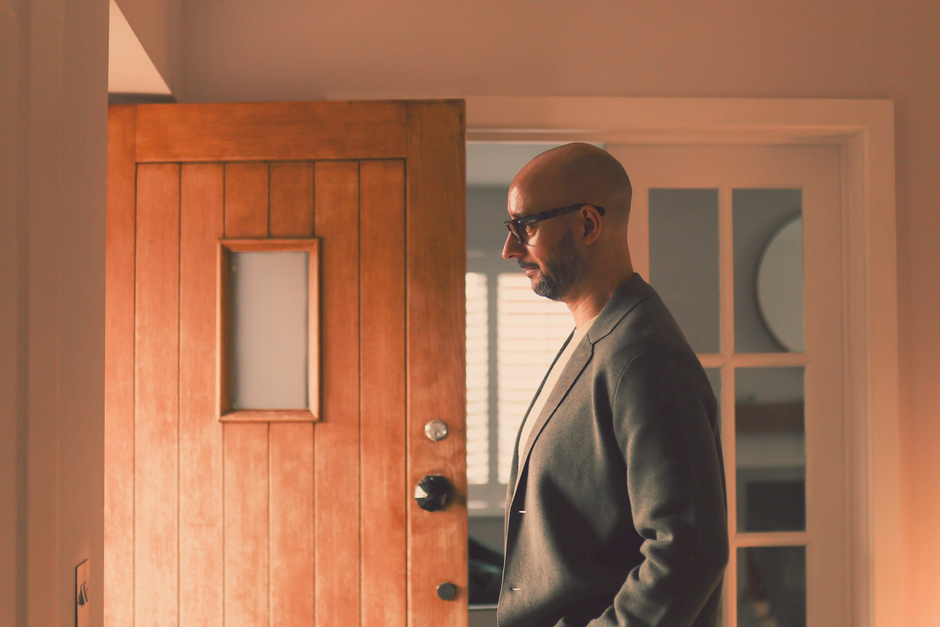 Justin Tate of The Exec Memo in a gray blazer stands near an open wooden door and a glass-paned door. Interior, neutral lighting.