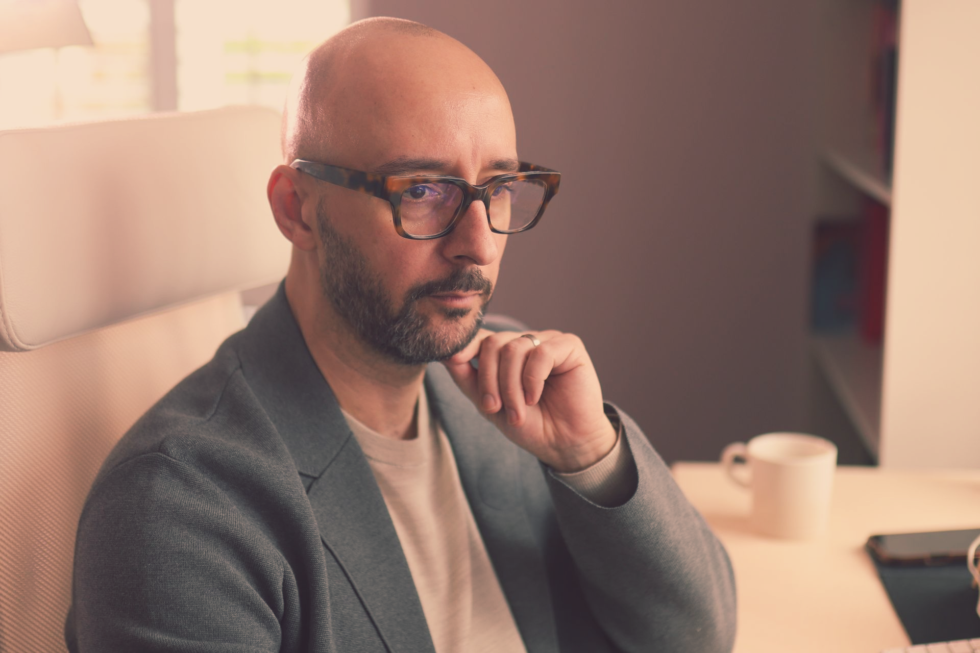 The ExecMemo's Justin Tate wearing glasses, resting chin, seated at desk, looking thoughtful.