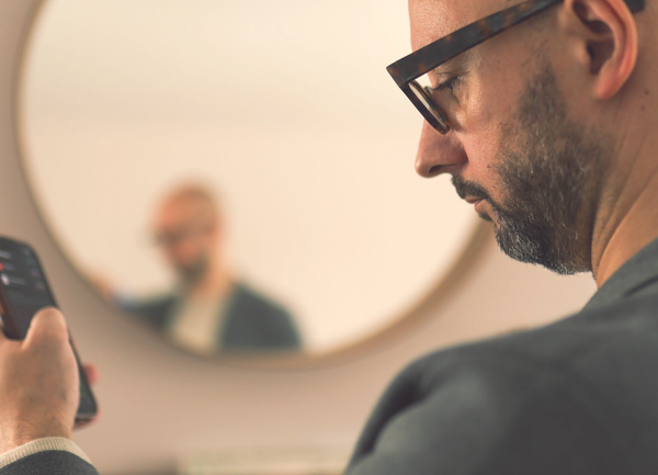 Justin of The Exec Memo in glasses looking at phone, reflection in mirror shows blurred image of him.