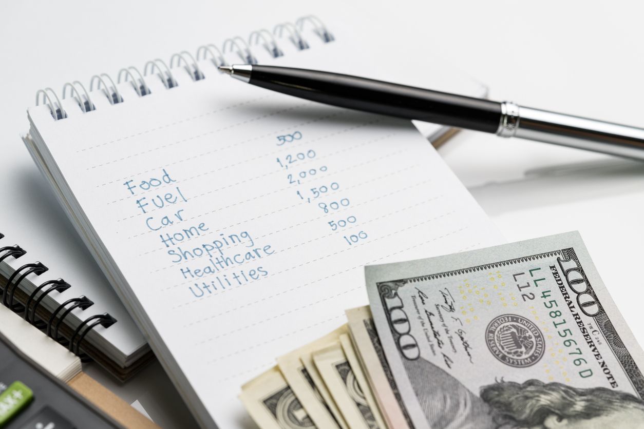 Notebook with budget notes, pen, and cash on a desk.