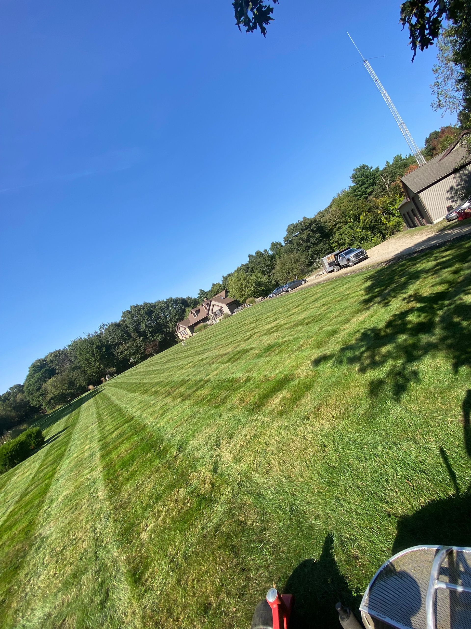 A lawn mower is cutting a lush green lawn in front of a house.