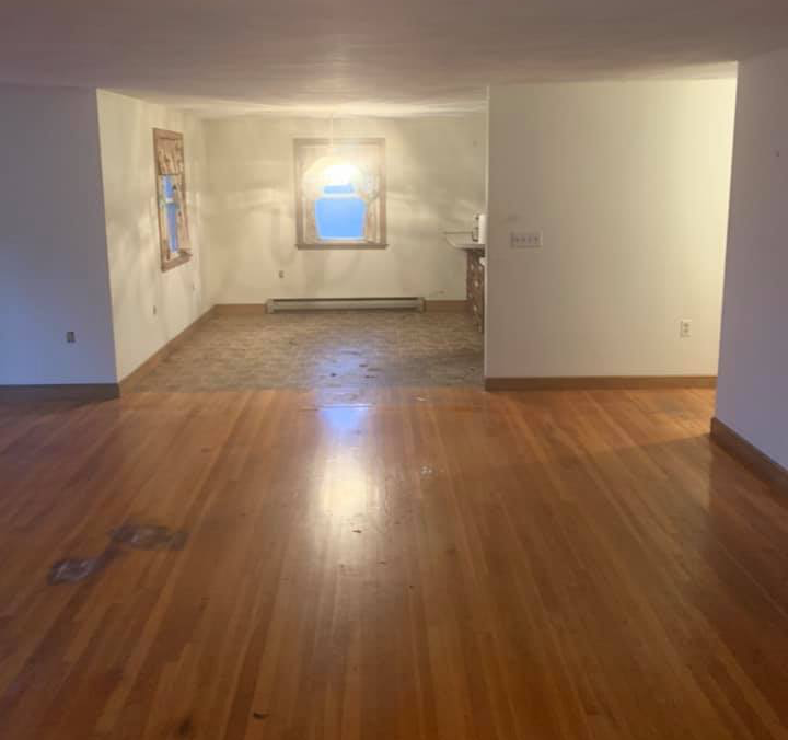 An empty living room with hardwood floors and white walls.