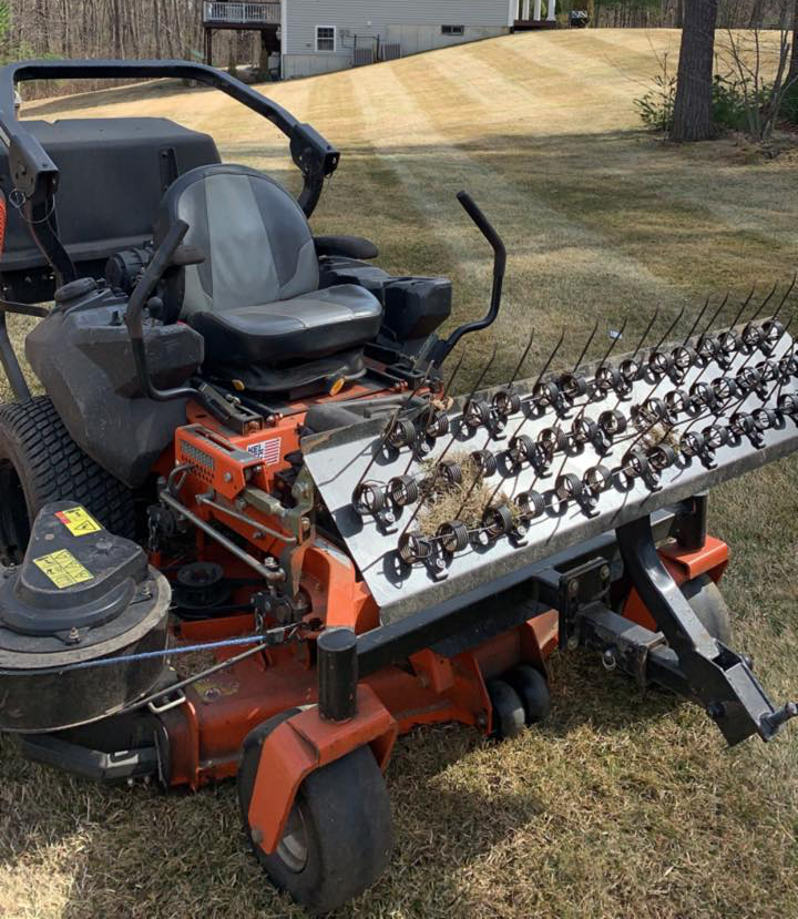 A lawn mower with a rake attached to it is parked in the grass.