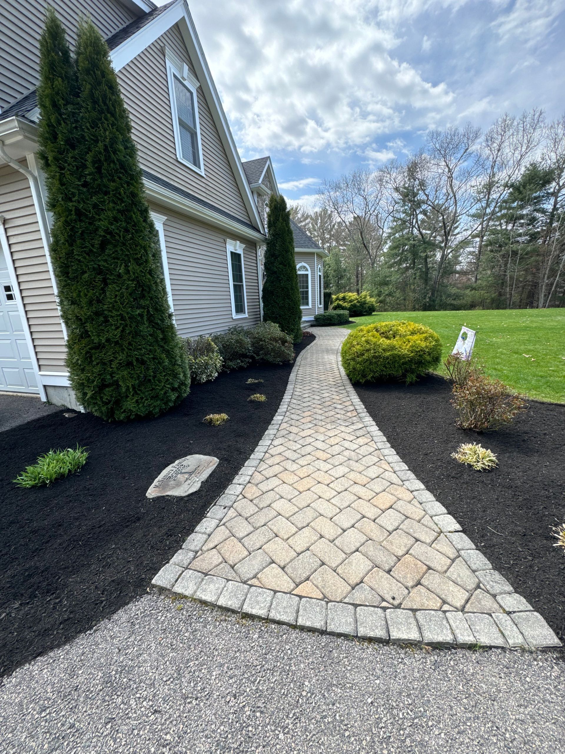 A brick walkway leading to a house with trees on both sides.