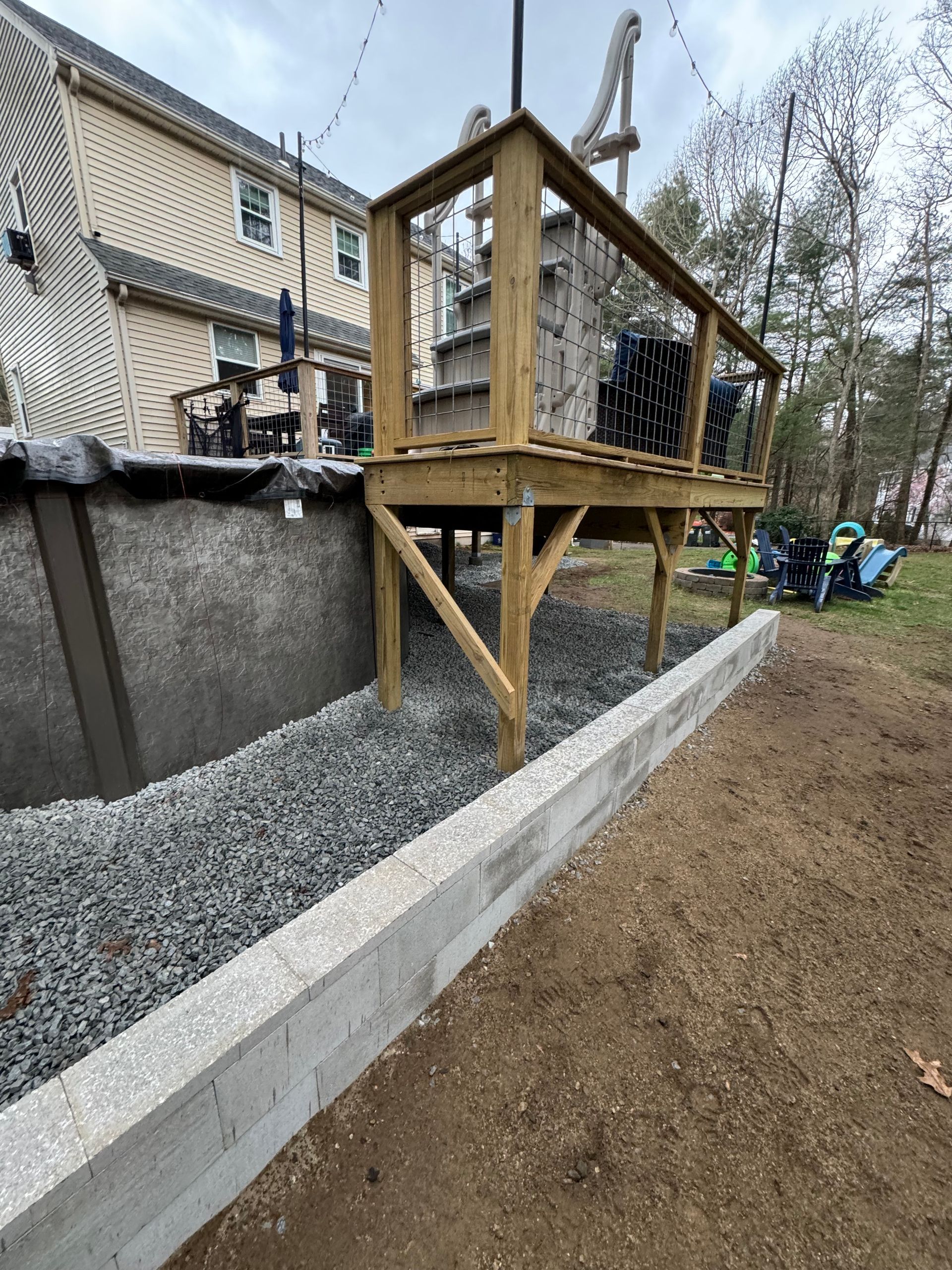 A wooden deck is sitting next to a pool in a backyard.