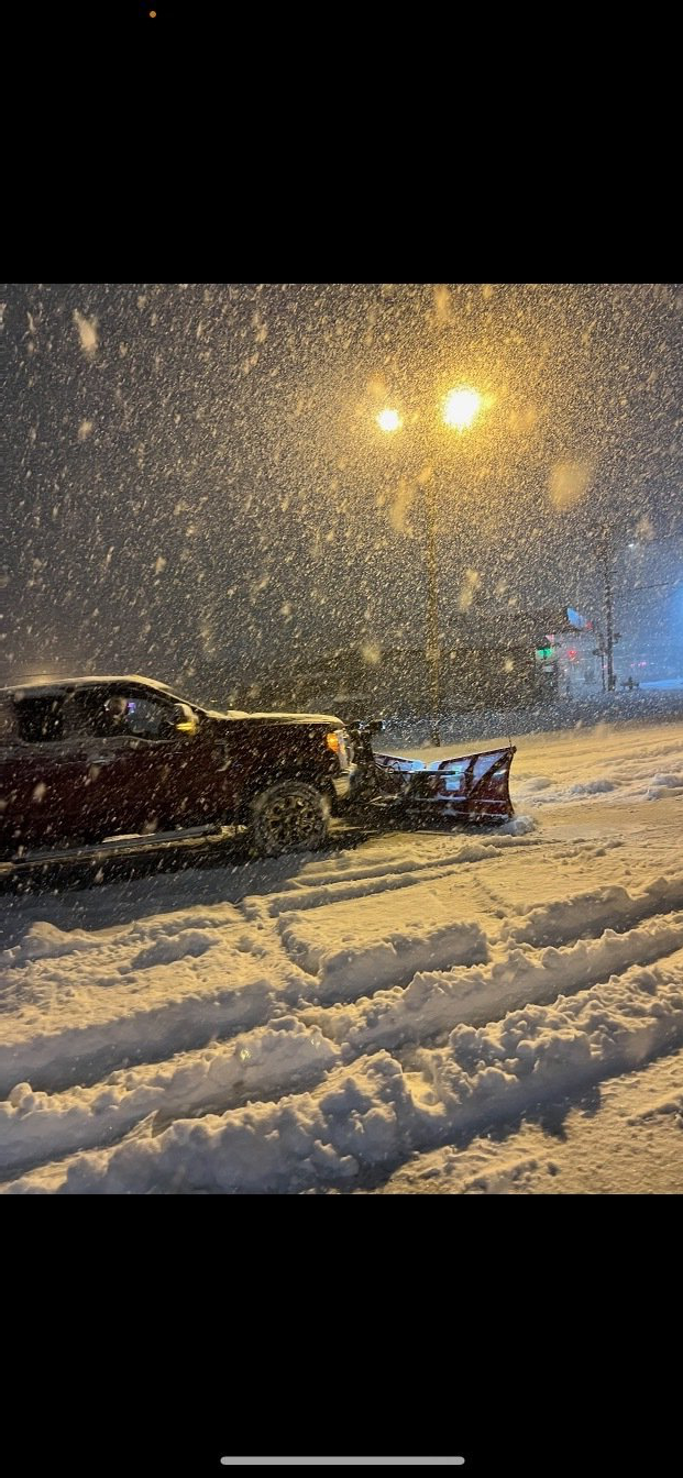 A snow plow is clearing snow from a parking lot at night.