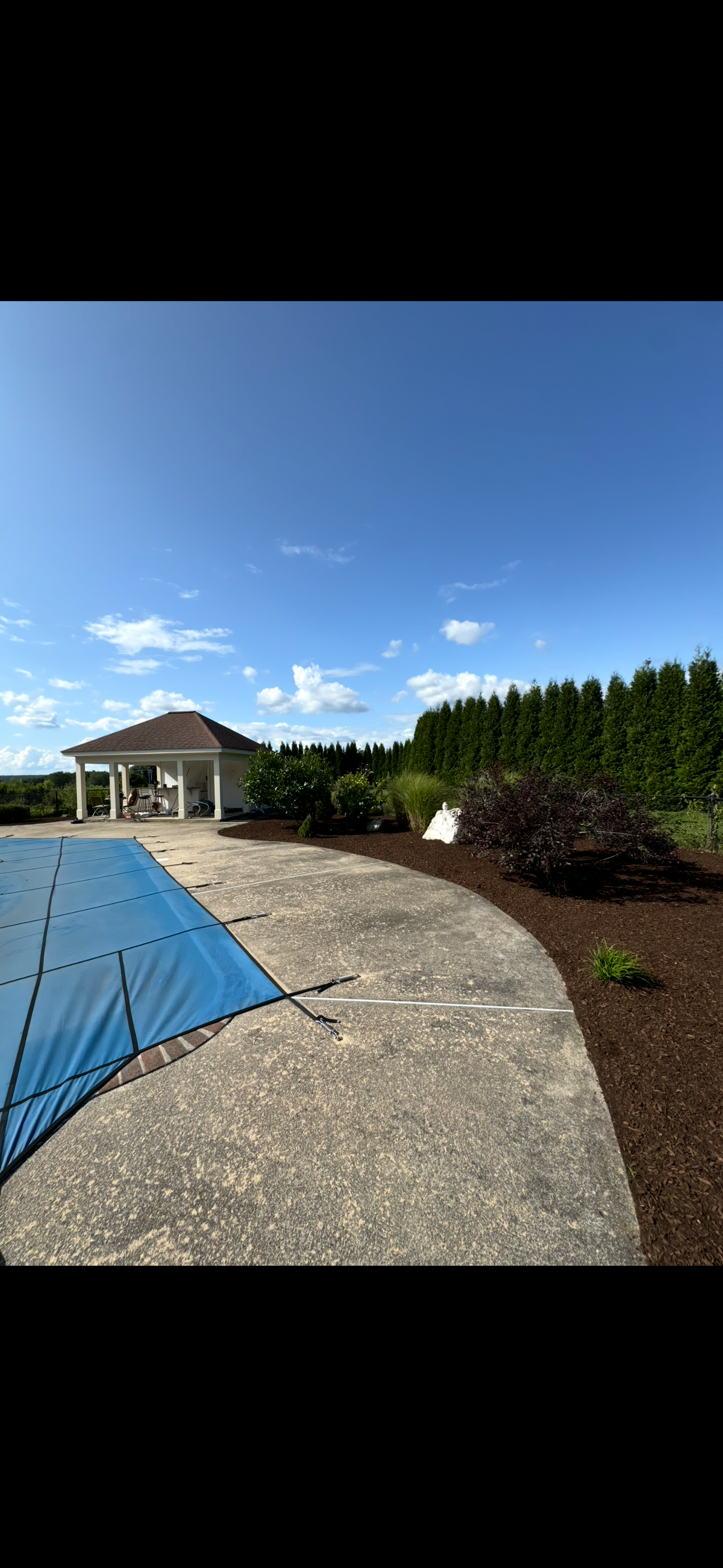 A swimming pool with a blue cover on it and a gazebo in the background.