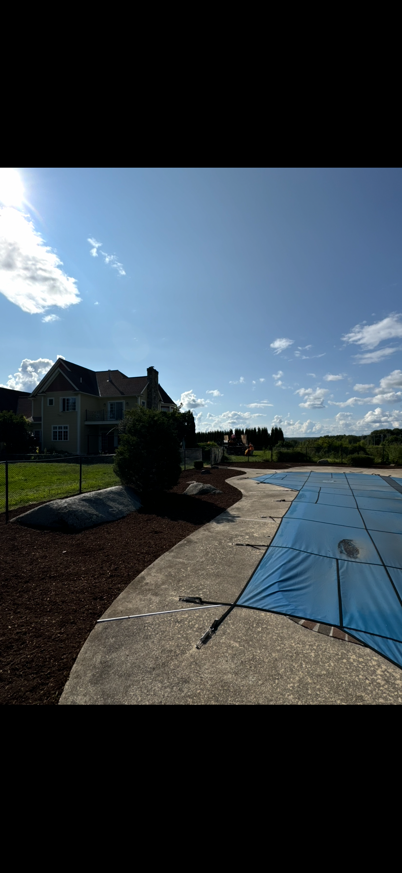 A large house is behind a swimming pool with a blue cover on it.
