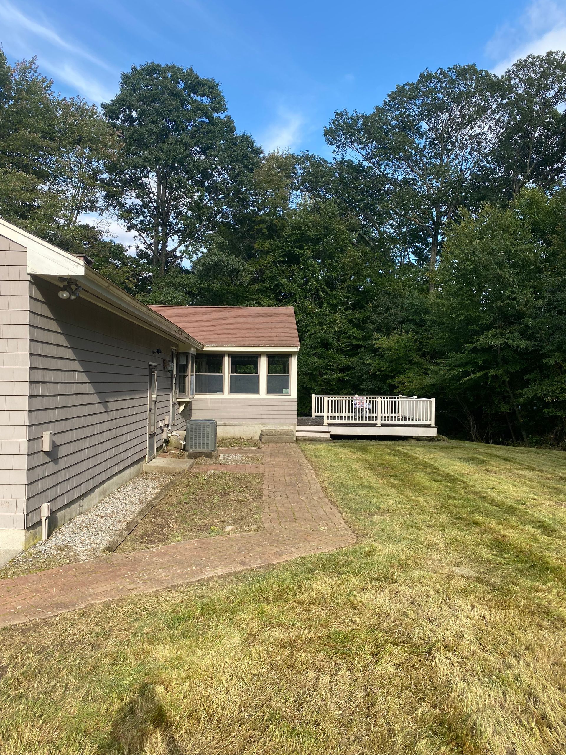 The backyard of a house with a deck and trees in the background.