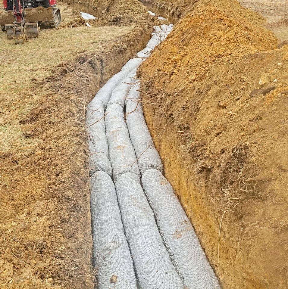 Freshly installed gray drainage pipes laid in a dirt trench on a construction site.