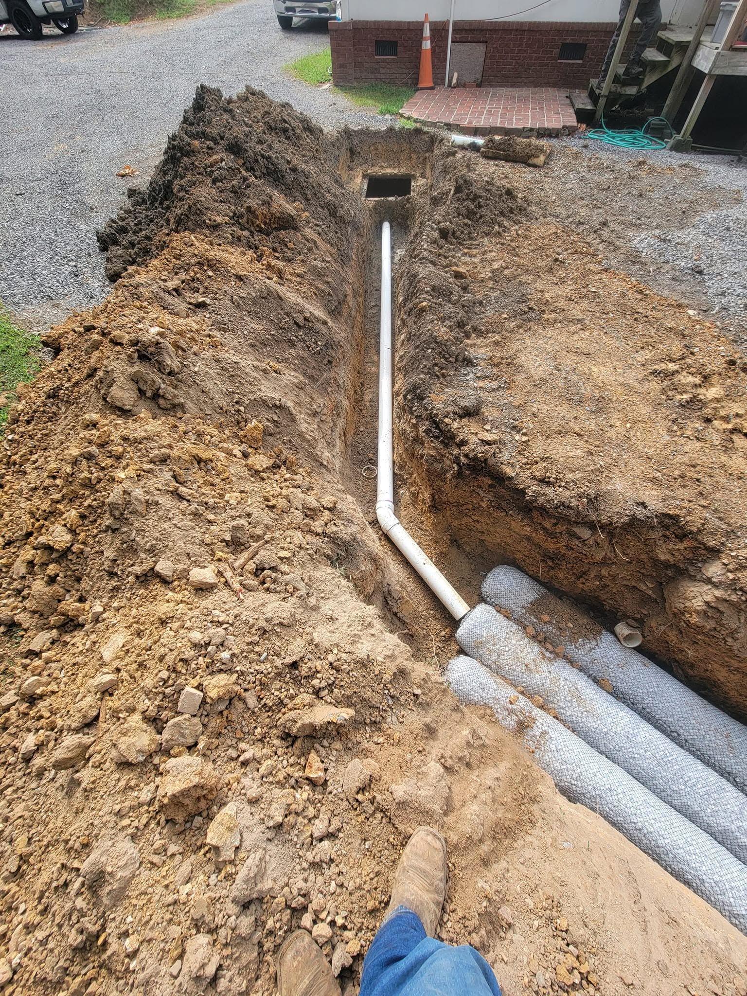 Freshly dug trench with white PVC pipe and a gravel yard beside a house